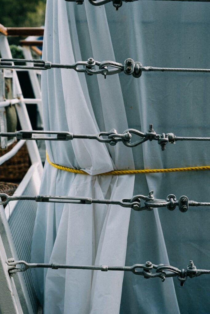 Detailed view of metal turnbuckles and ropes on a ship with white cloth background, showcasing marine equipment.